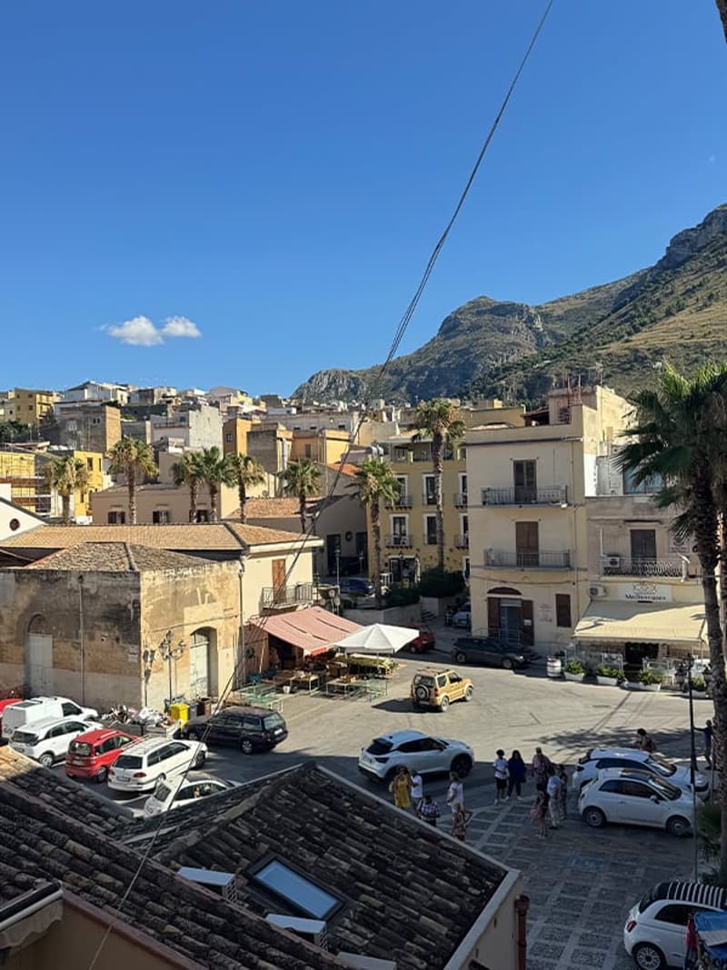 aerial view, parking lot, many cars, buildings, mountains in the distance, sunny day, few people walking around, palm trees, awnings on buildings