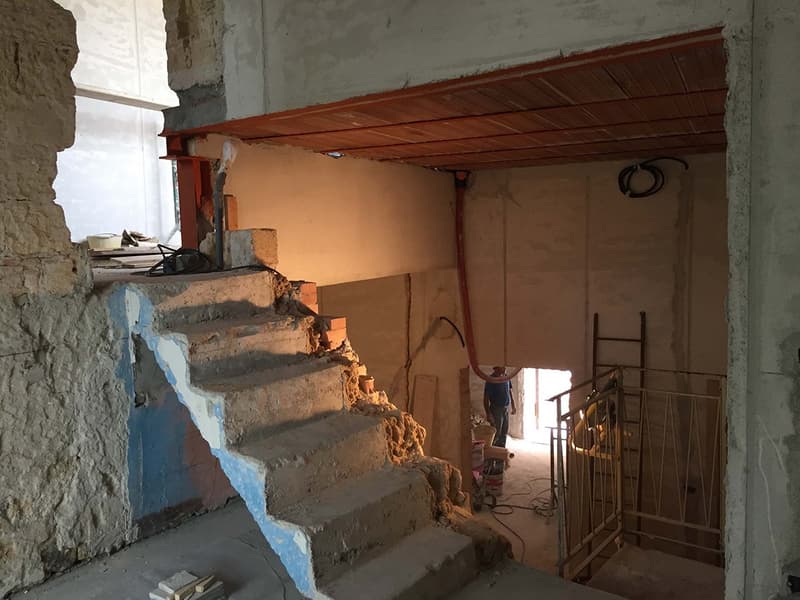 Stone and brick wall, concrete steps, blue paint, ladder, workman, tools, and construction materials