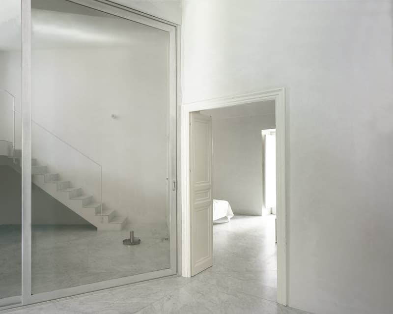 white interior, large glass doors, glass wall reflecting staircase, minimal furniture, large open space