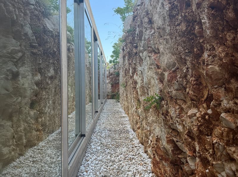 Pathway between walls, made of small rocks, with large glass windows and gray frames
