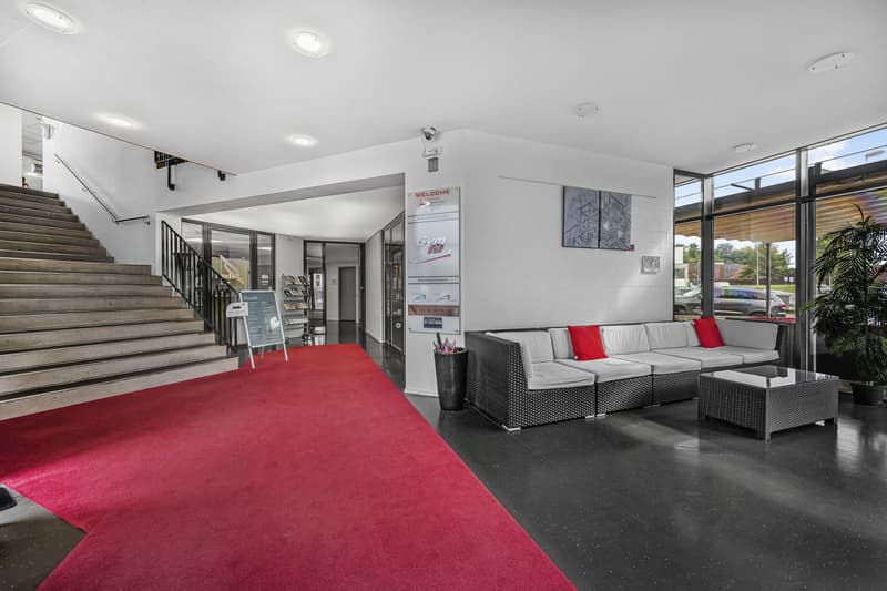 Red carpet, stairs leading to the upper floor, glass doors, couch, coffee table, potted plant, welcome sign