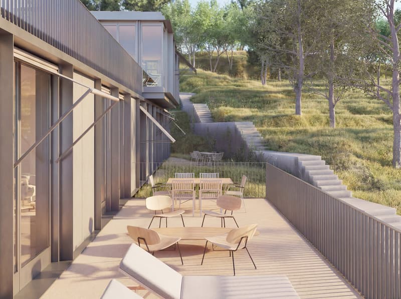 modern building with glass walls, outdoor terrace with dining area, steps leading to a grassy hill