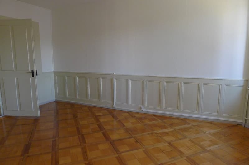 Empty room, white walls, wooden floor, and paneling. An open door on the left.