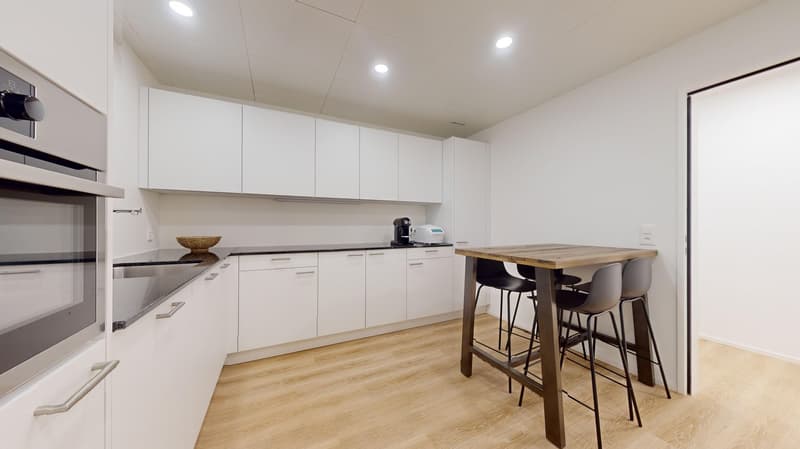 modern kitchen with a wooden table, white cabinets, wooden floor, black countertops, built-in oven and coffee machine
