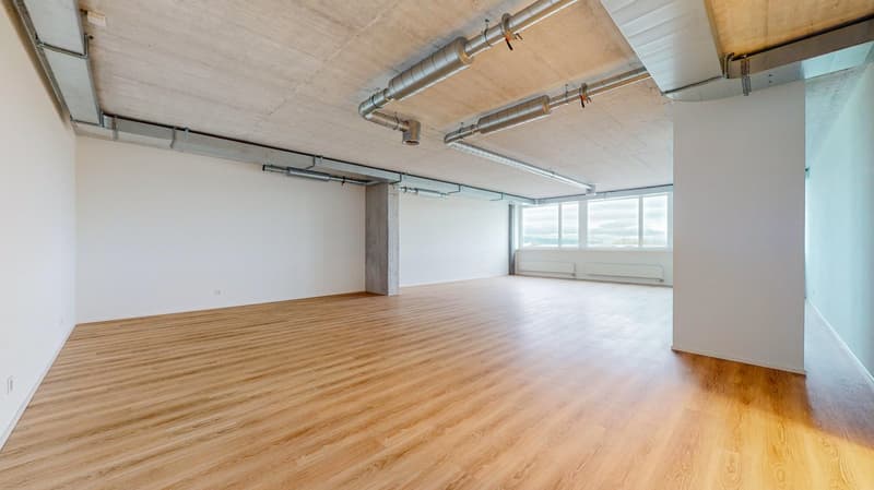 Empty room, large windows, concrete pillar, exposed pipes, hardwood flooring