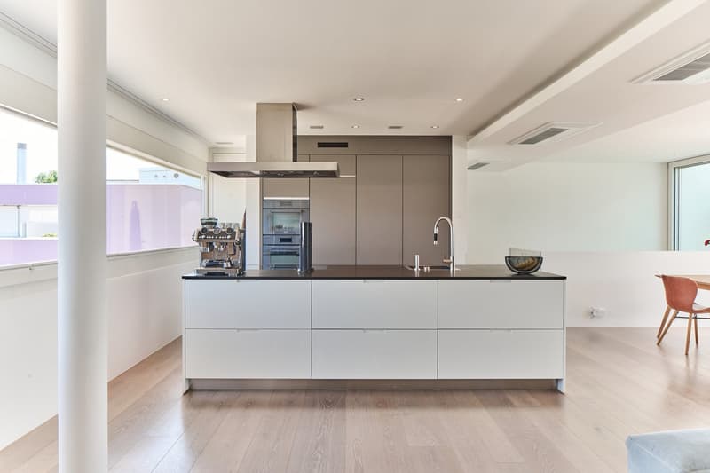 Spacious modern kitchen with white cabinets, black countertops, built-in appliances including a dishwasher, and a coffee machine on the counter.