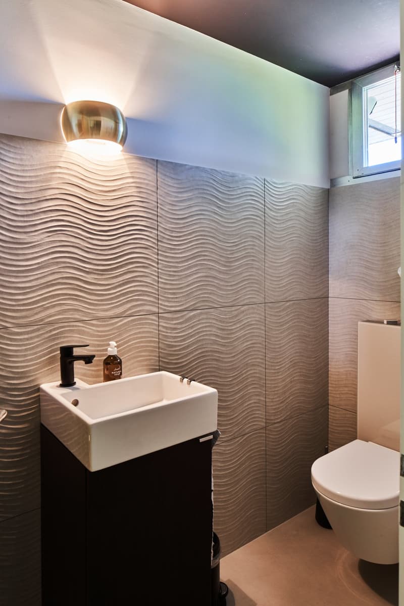 white sink, wall-mounted toilet, patterned walls, wall light, soap dispenser