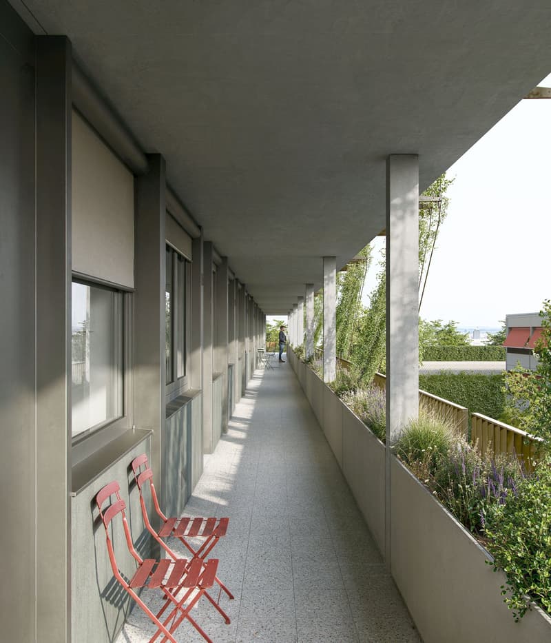 Elevated walkway, red chairs, large columns, greenery, windows
