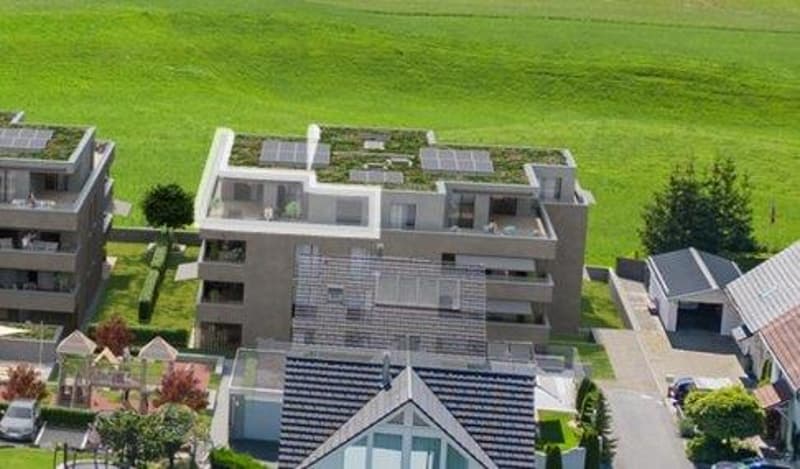 Aerial view of a residential building complex with solar panels on the roofs, surrounded by greenery and a playground.