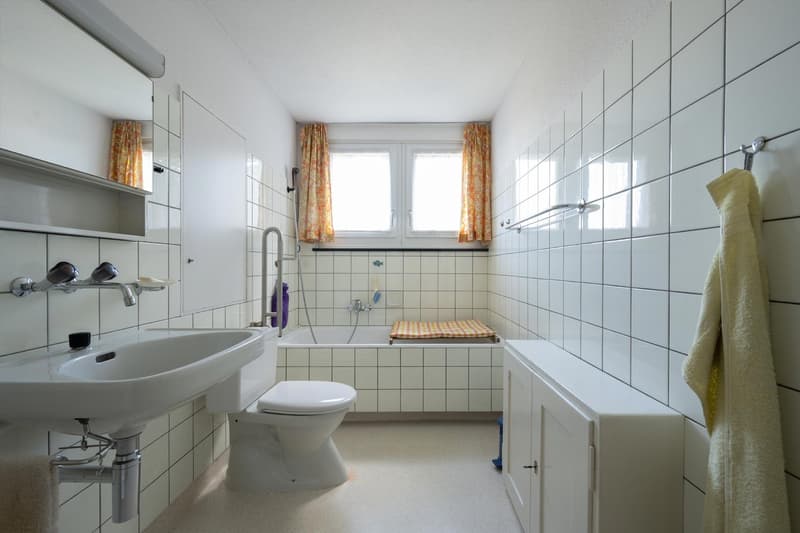 tiled walls, white porcelain sink, white ceramic toilet, white bathtub, white cabinetry, window with yellow curtains, silver shower head