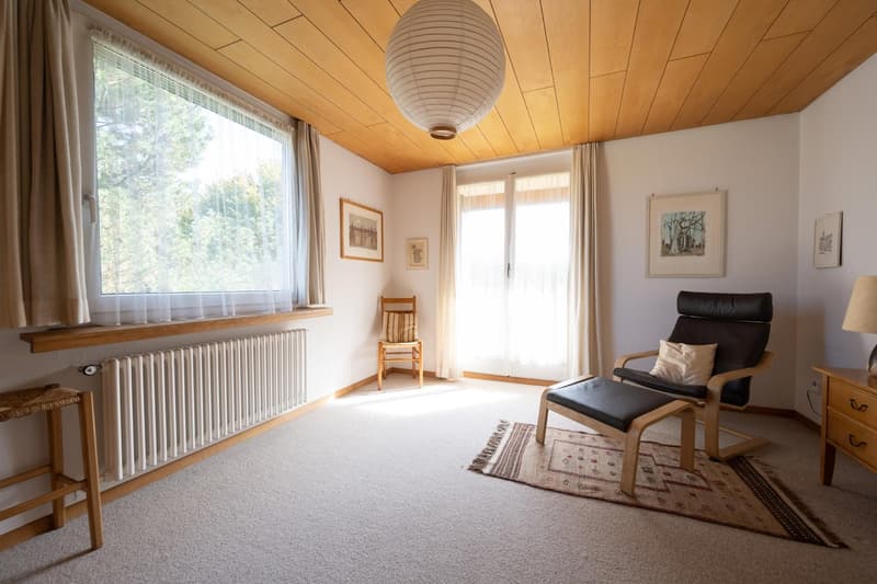 Empty living room, white radiator, large window, wooden ceiling, white walls, rug, armchair, lamp, wooden chair