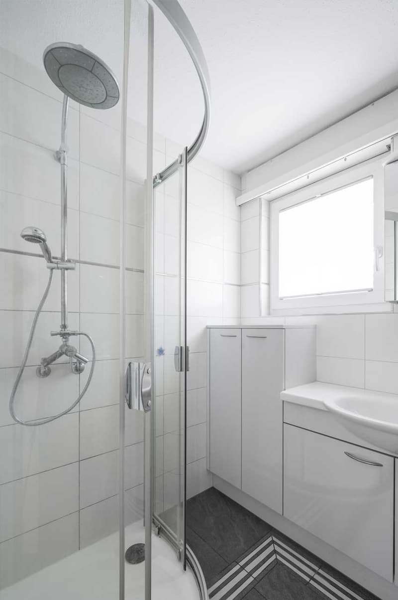 modern bathroom, shower stall, white tiles, shower head, sink, cabinets, white countertop, window