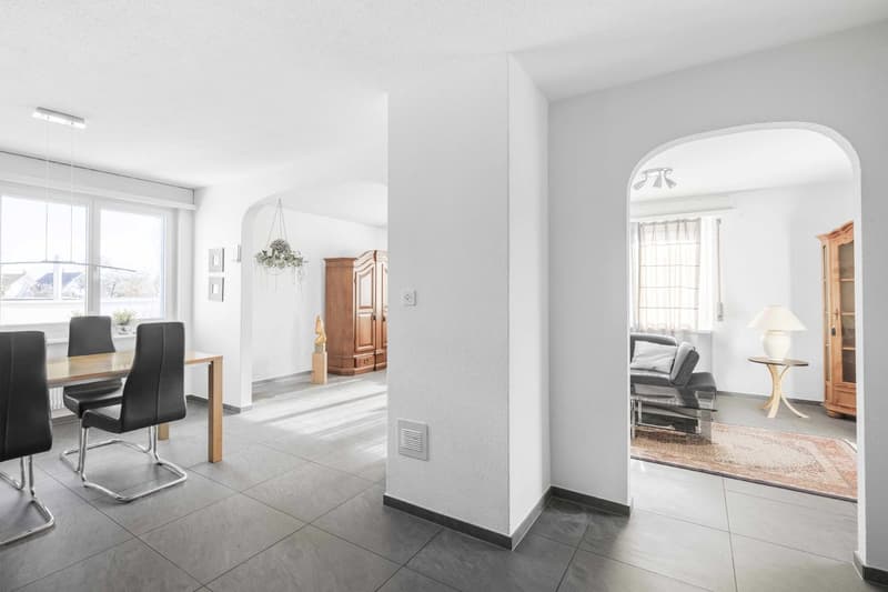Dining room with wooden table and chairs, living room with couch and armchair, carpet on floor, large window
