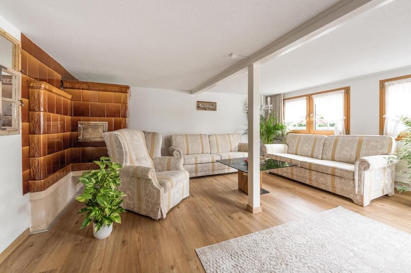 wooden floor, large windows, wooden column, beige and white striped sofa, armchair, potted plant, rug