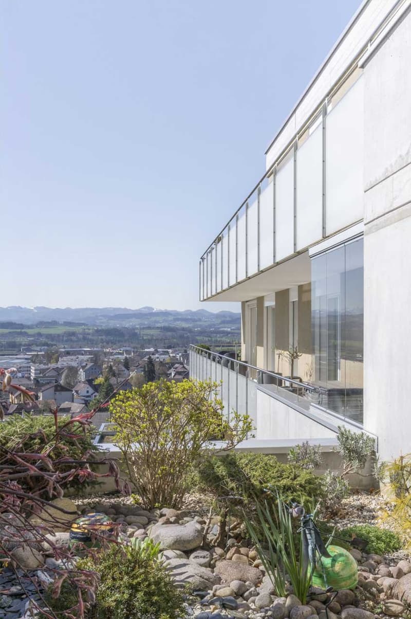 modern white building, large glass windows, balcony, garden with rocks and plants