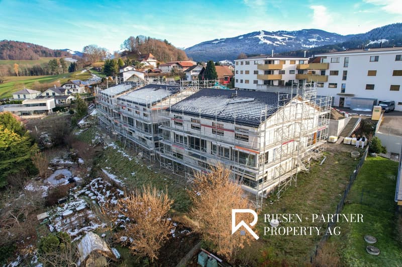 Aerial view of a new construction building with scaffoldings on the exterior. In the background are other houses and a mountain landscape.