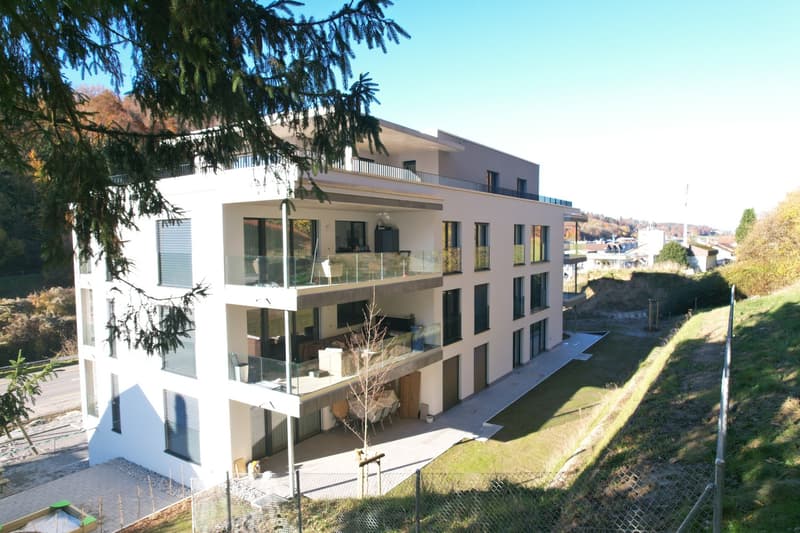 modern apartment building, white exterior, glass windows, multiple balconies, parking area, green surroundings