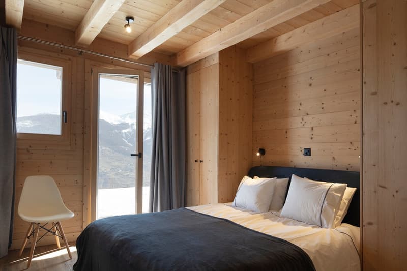 bedroom with wooden walls, bed, pillows, chair, glass door, curtains, mountain view