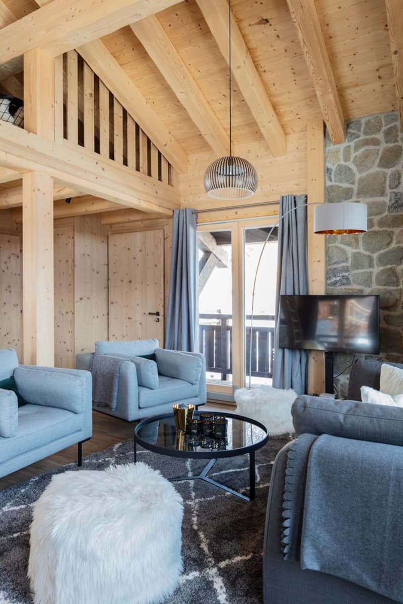 living room with wooden beams, stone wall, glass door, large windows, blue couches, coffee table, lamps, TV, carpet