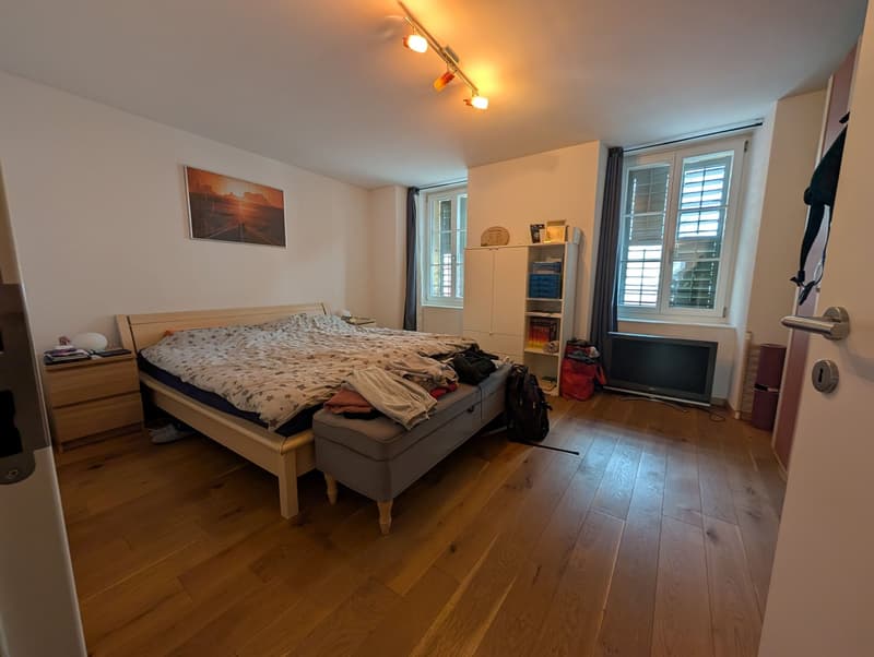 bedroom with bed, nightstand, TV, cabinet, storage bench, window, hardwood floors
