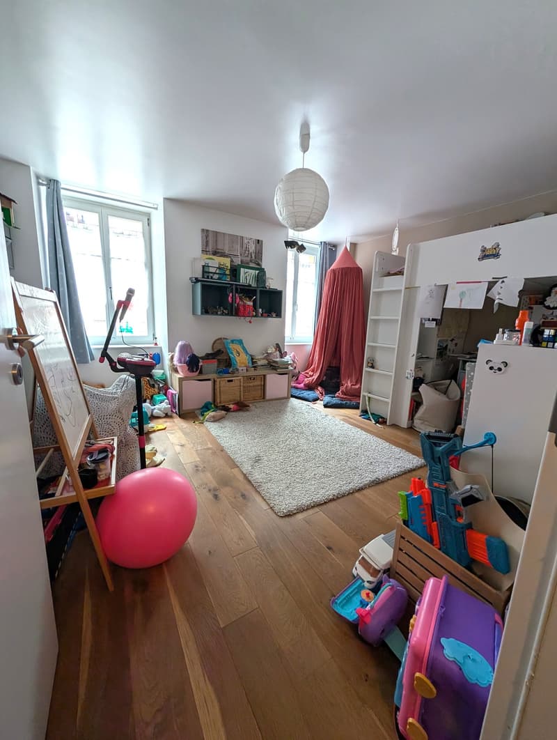 kids room with wooden floor, playmat, toy cars, dollhouse, bunk beds, loft bed, desk, play tent, bookshelf, toys, exercise bike, lamps, windows with curtains