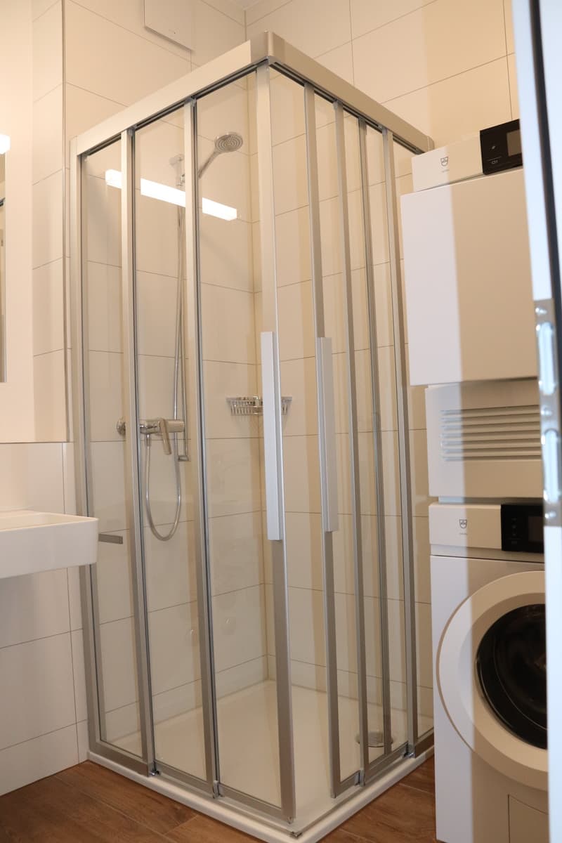 large shower, tile walls, white sink, white washer machine