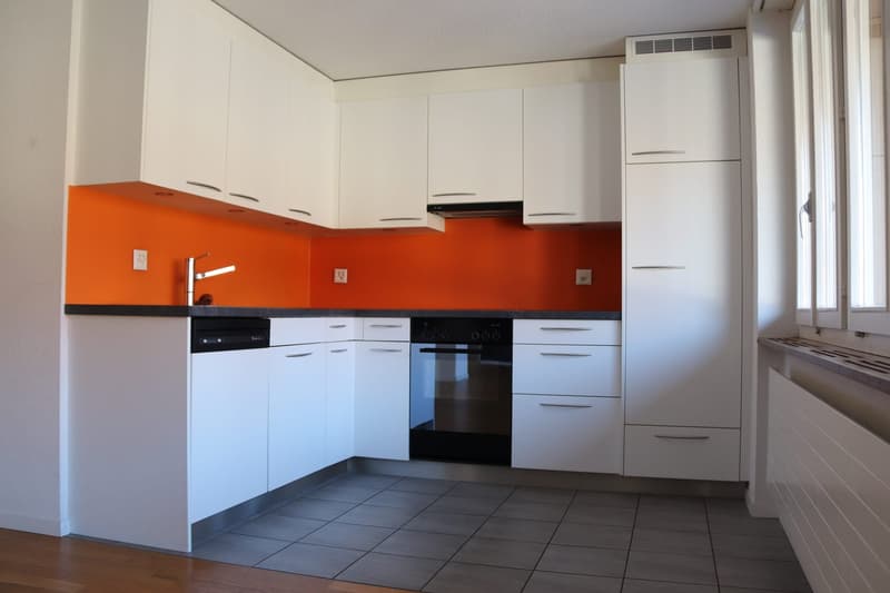modern kitchen with white cabinets, orange backsplash, black appliances, tiled floor