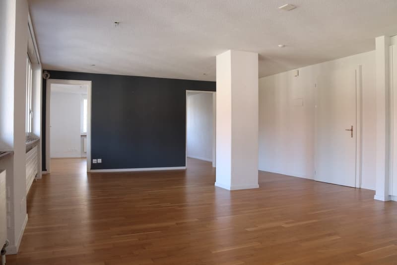 Empty room with wooden floor, white walls, black wall, white doors, power outlets, and a pillar.