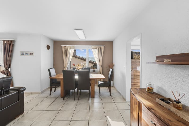 Dining room with wooden table, black leather chairs, white tiled floor, wooden cabinet, wall art, glass window with curtains, lamp, view of outside