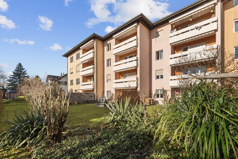 modern apartment building, beige and pink facades, multiple balconies, landscaped garden with green lawn and plants