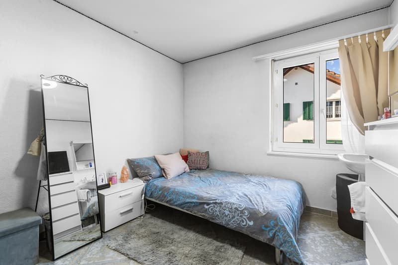Small room with single bed, window, mirror, cabinet, nightstand, rug, lamp