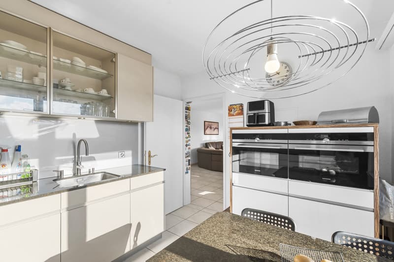 Modern kitchen with stainless steel sink, granite countertops, white cabinets, double oven, glass cabinets, and a spiral pendant light.
