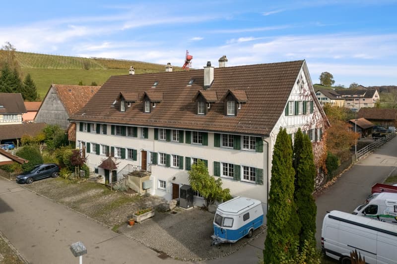 3 story house, brown roof, green shutters, white walls, multiple windows, balcony, garden, cars parked in front