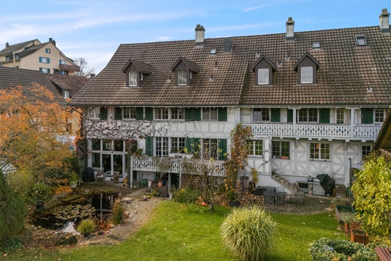 3 story house, brown roof, white walls, green shutters, balcony, garden, pond