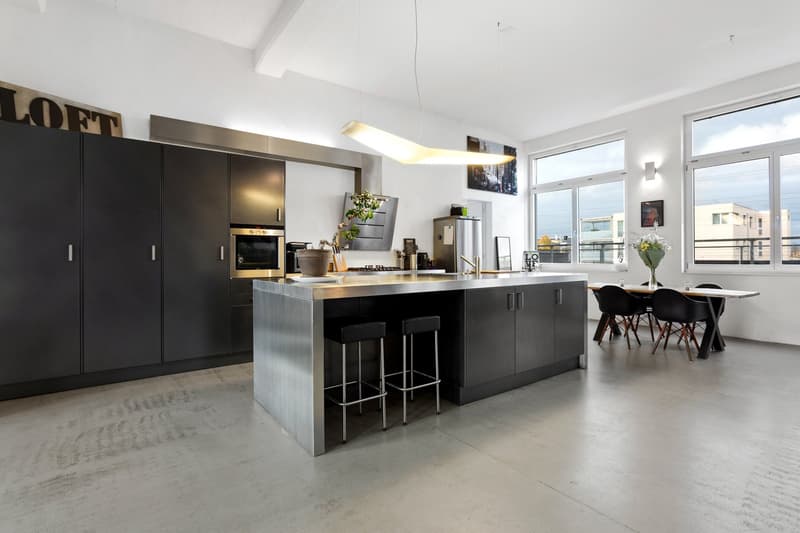 modern kitchen with island, large windows, stainless steel appliances, black cabinets, concrete floor