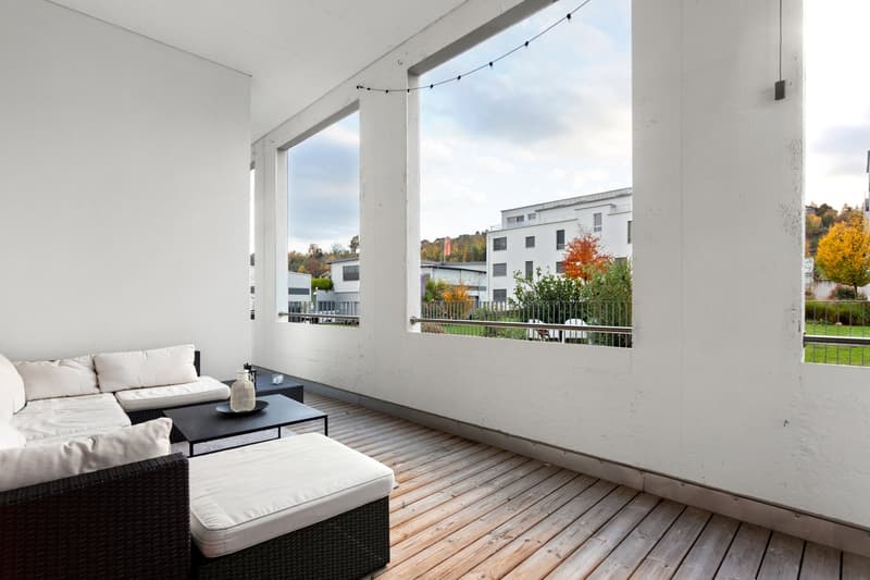 Balcony with wooden floor, white walls, large windows, outdoor furniture, view of the outside