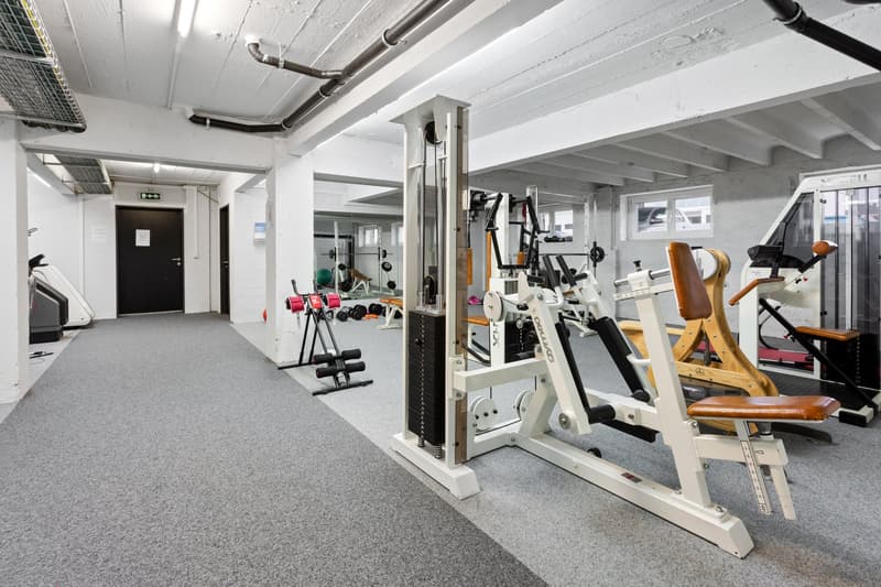 gym room with various exercise equipment, gray carpet, white walls, ceiling with pipes