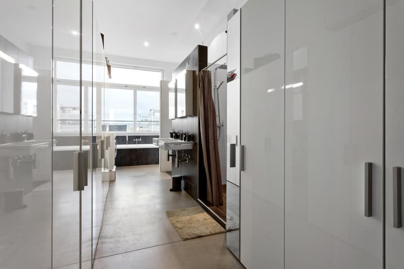modern bathroom with white walls, glass partitions, concrete floor, bathtub, double sink, shower, and a rug