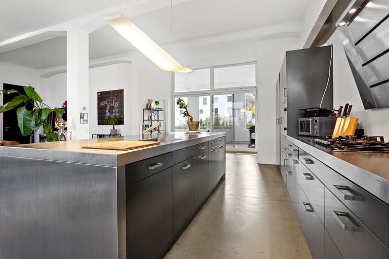 modern kitchen with stainless steel island, black cabinets, white walls, large windows, plants, microwave, gas stove, sink