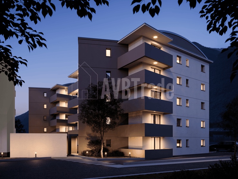 Modern multi-story residential building with balconies and windows, illuminated in the evening, surrounded by greenery.