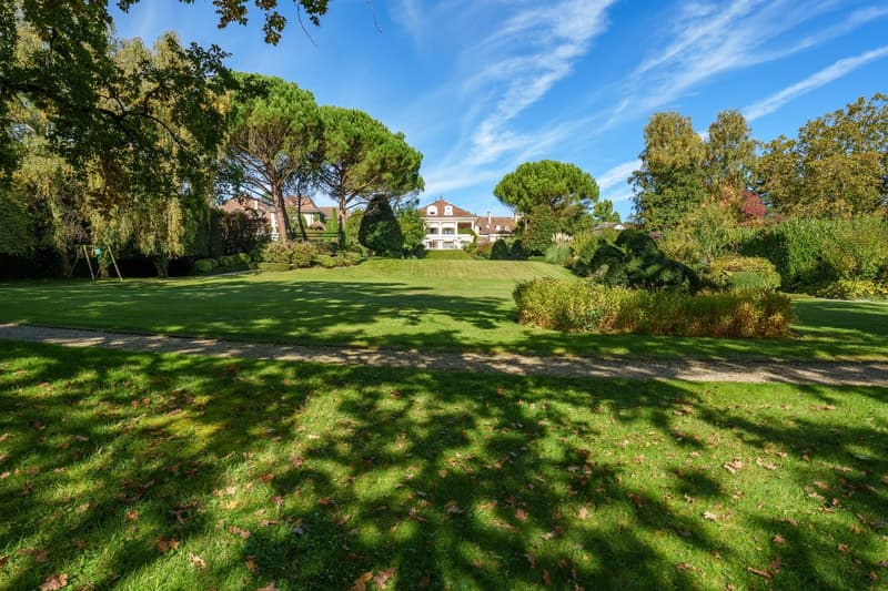 Large well-kept lawn, several trees, large white house in the background