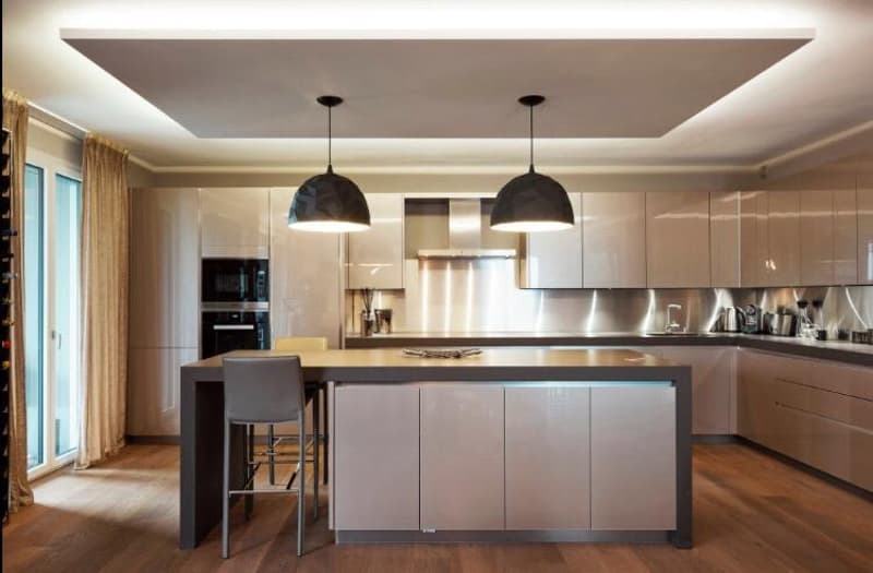 Modern kitchen with island, high ceilings, wooden floors, stainless steel countertops, built-in oven, open cabinets, pendant lights, large windows, glass doors to balcony