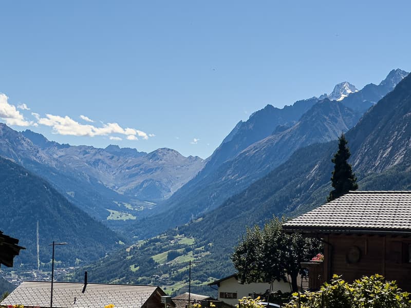 Mountain valley with snow-capped peaks, wooden chalets, and a valley floor.