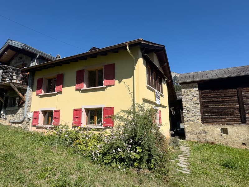 Yellow 2 story house, stone and wood construction, red shutters, sloped roof, garden