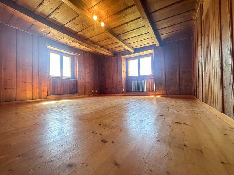 Large room with wooden walls and floors, two windows, exposed wooden ceiling with ceiling lights