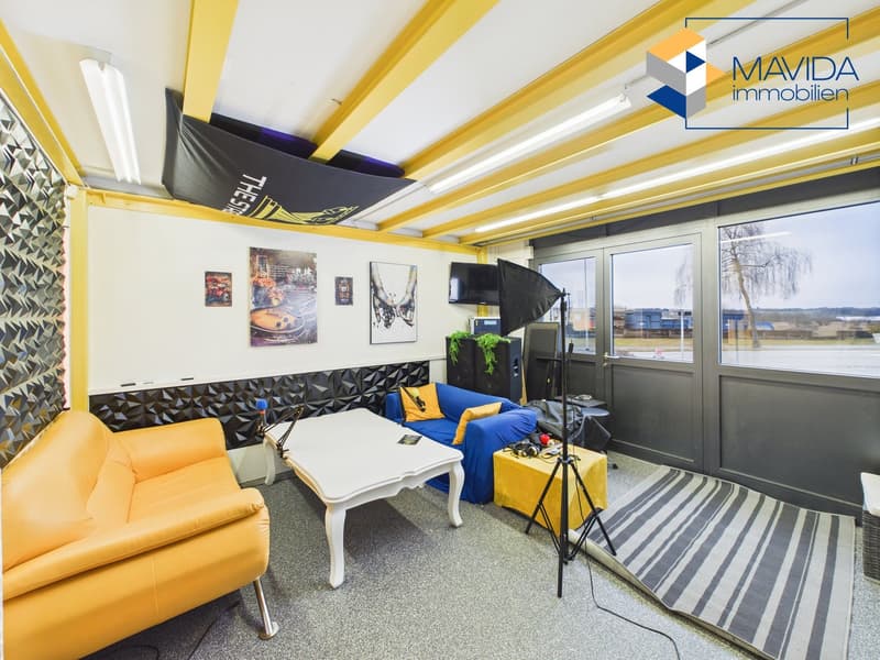 Living room with gray walls, gray floor, light blue couch, yellow couch, white table, black television, white ceiling with lighting.