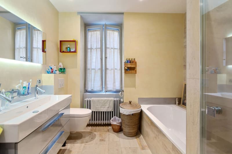 white bathtub, modern sink, two shelves, radiator, window with white curtains