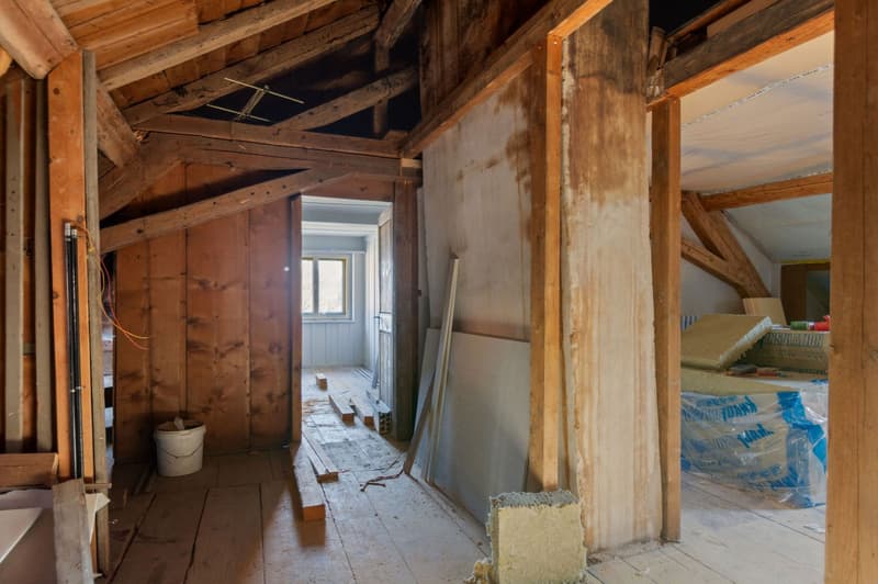 Wooden beams, wooden flooring, white painted window frame, stack of insulation material, materials scattered on the floor