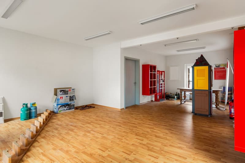 empty room, wooden floors, white walls, fluorescent ceiling lights, gas cylinders, storage boxes, shelves, fire extinguisher, wooden toy house