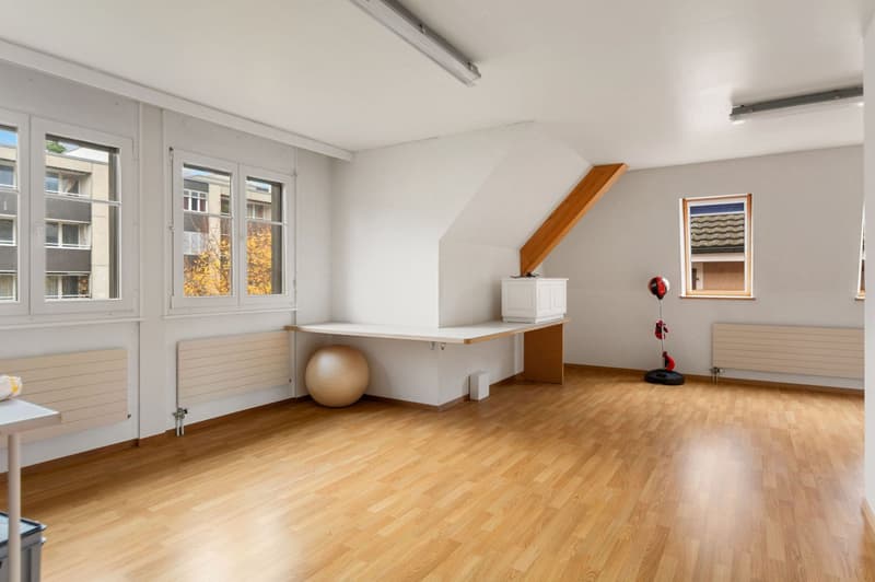 empty room, white walls, hardwood floor, two windows, sloping ceiling, desk, punching bag, fitness ball